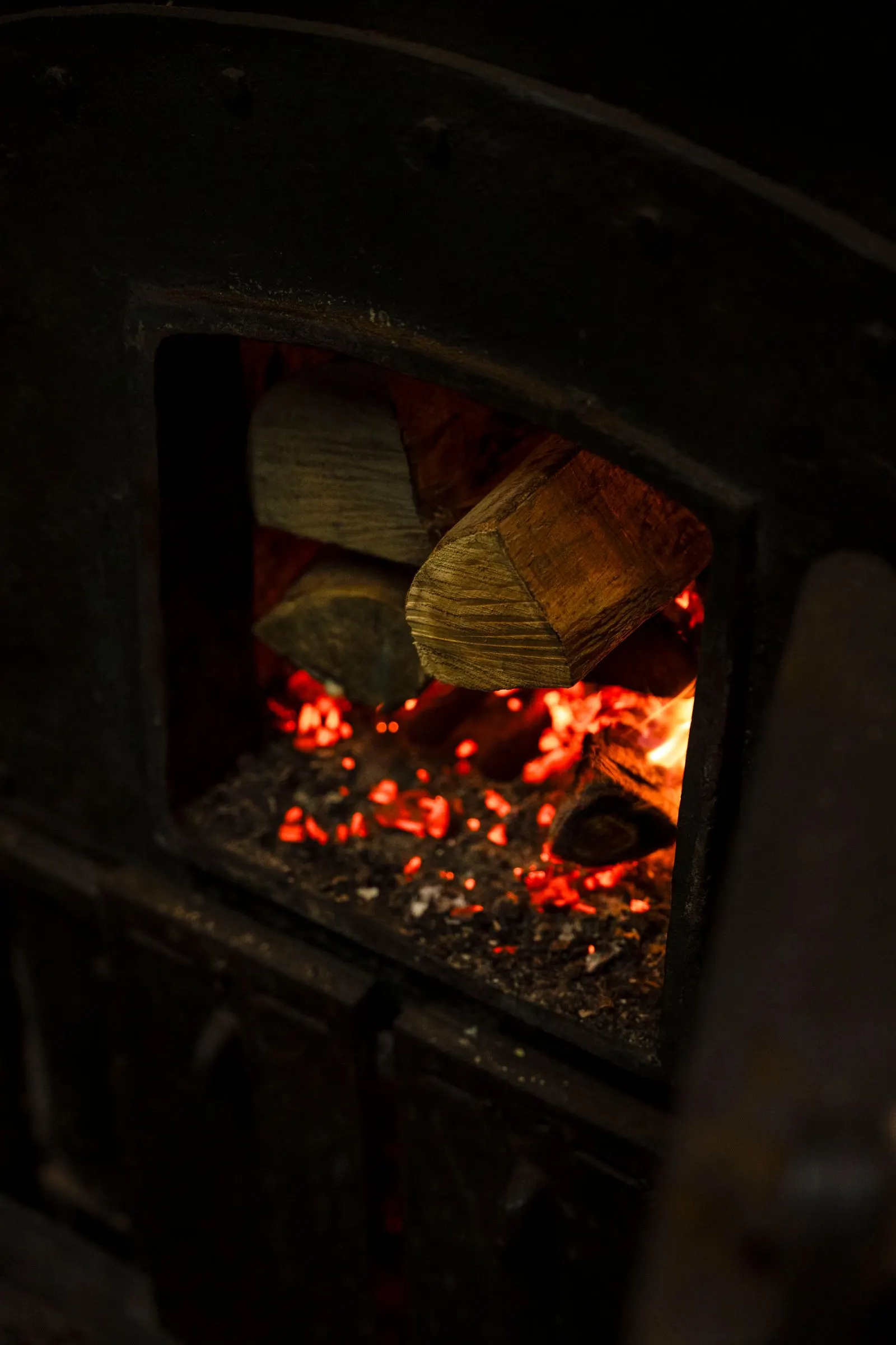 Braises rouges et bûche vues par la porte ouverte d'un poêle en fonte